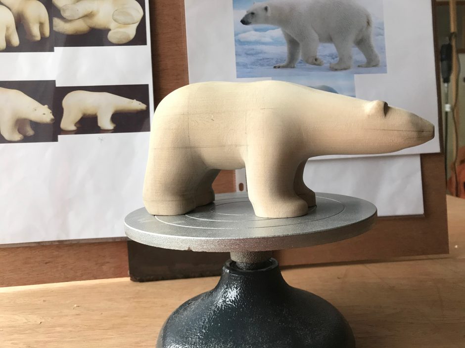 Side view of wooden model of Polar bear standing on metal turntable, with reference images in the background