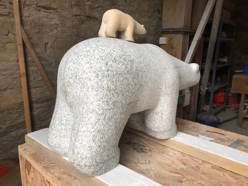 Rear side view of work in progress on granite carving of Polar bear with wooden scale model resting on its back