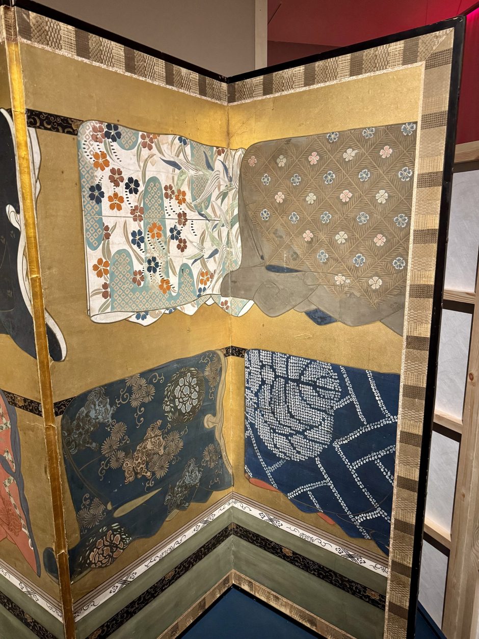 Detail of historical Japanese folding screens, 4 different fabric designs on kimonos which are hung up.