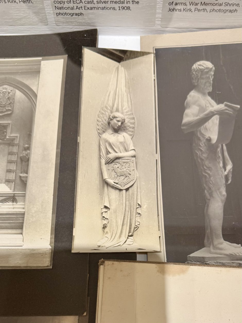 Display of photographs, in the centre a photo of an angel designed to fit into a corner holding a shield.