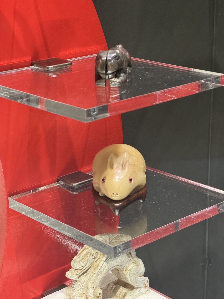 Carving of a rabbit in white stone with a red background, the eyes of the rabbit have red stones set in it them, it is on a clear museum shelf