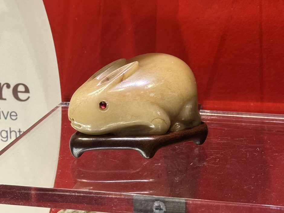 Carving of a rabbit in white stone with a red background, the eye of the rabbit has a red stone set in it