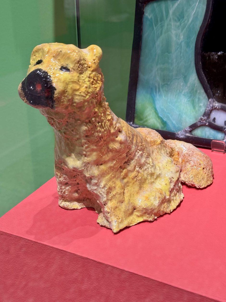 Oblique front view of dog made from ceramic, it is glazed yellow with a black nose and eyes