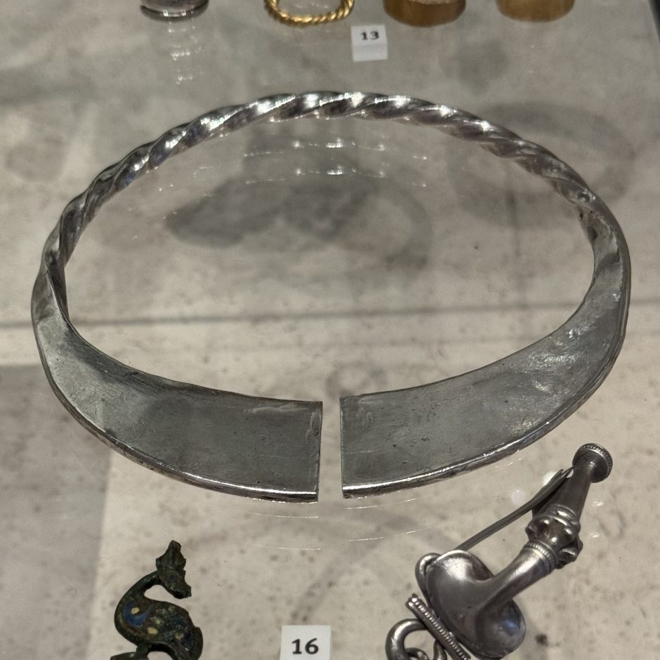 Image of a piece of jewellery made in silver, the back is twisted and at the front there are 2 flattened areas, there is an opening at the front