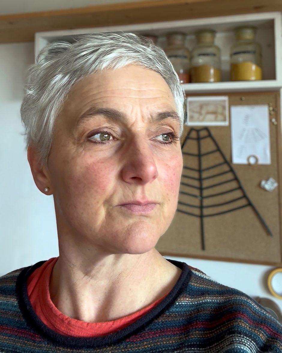 Portrait with grey hair. In the background there is a shelf which has jars of raw pigment on it, there is also a pinboard in the background